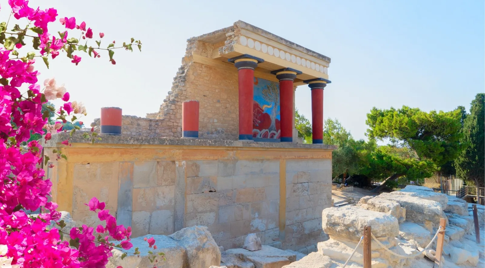Restored upper storey at Knossos with red columns and the bull fresco, seen past flowering bougainvillea