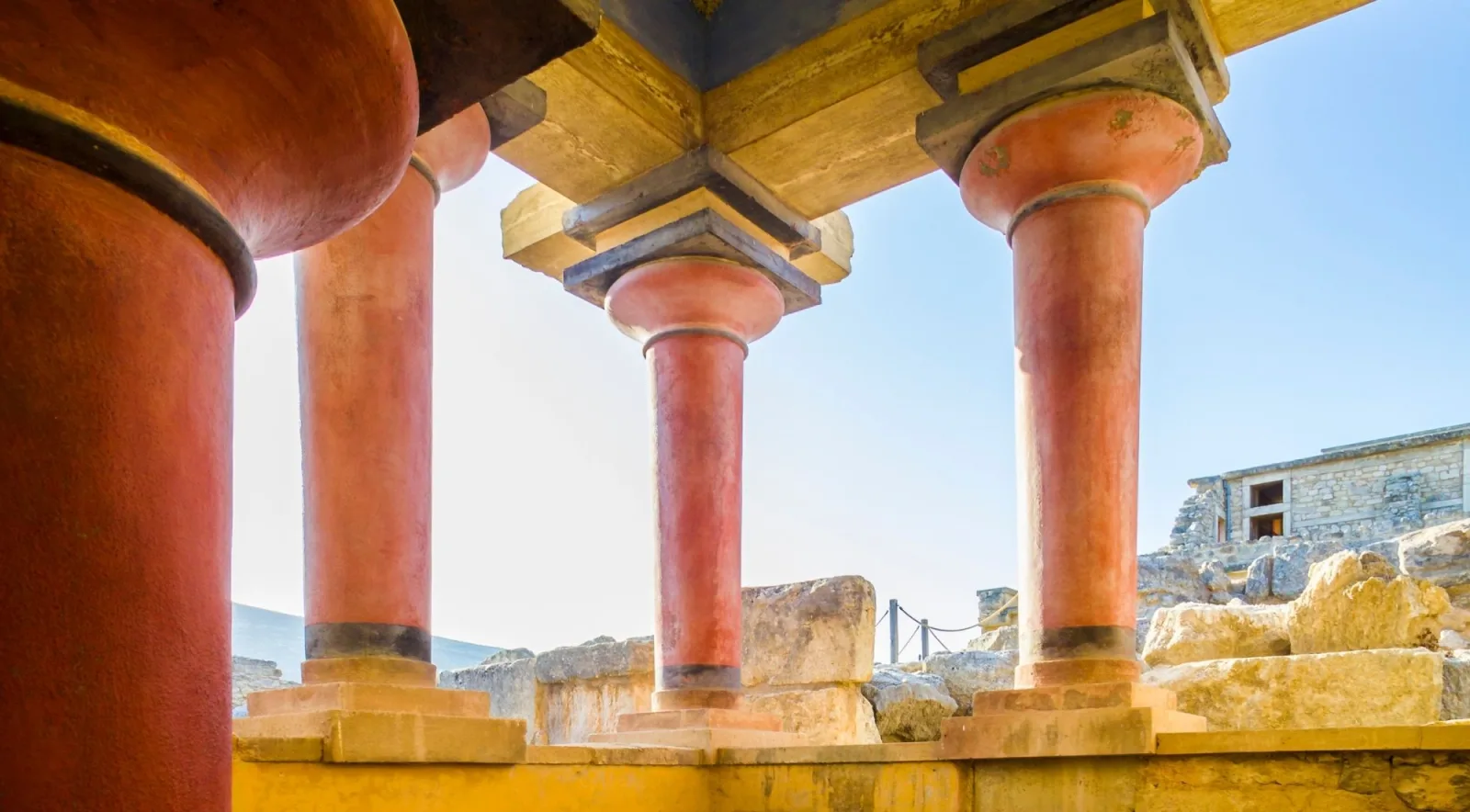 Row of red Minoan columns photographed from below against a blue sky at Knossos