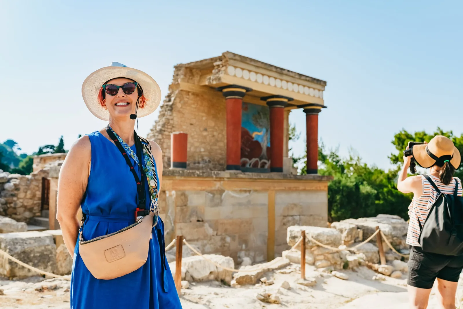 A visitor in a sun hat standing in front of the red Minoan columns of the restored facade at Knossos