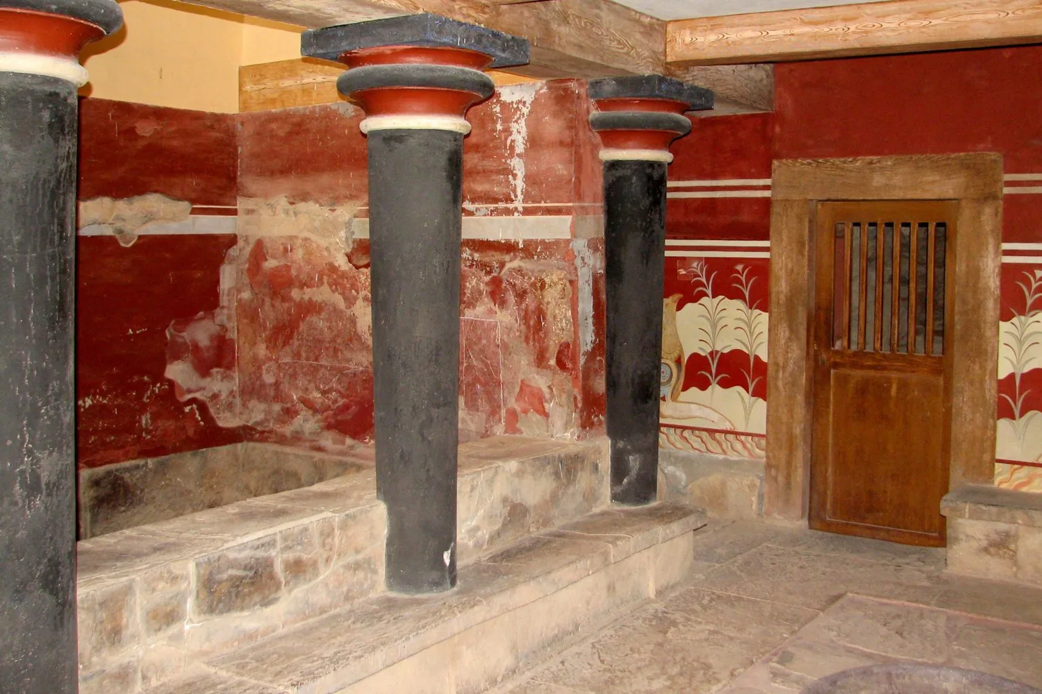 A dark Minoan column beside a deep red painted wall in the restored quarter at Knossos